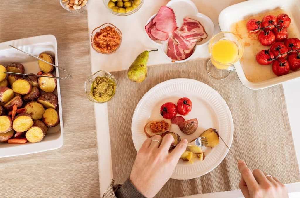 Top-down view of a vibrant brunch spread featuring roasted potatoes, tomatoes, cold cuts, and fresh juice.